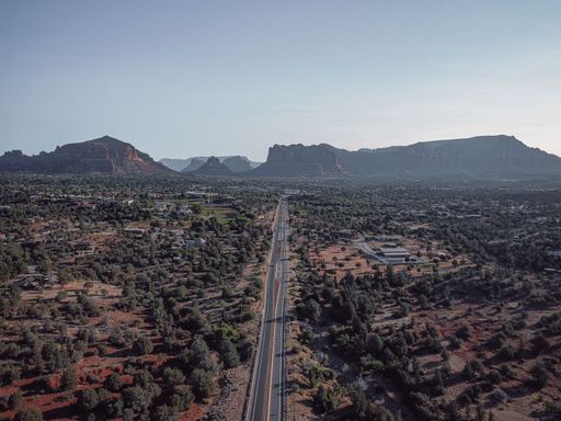 An aerial shot of a long road with mountains and greenery in the background under clear blue sky