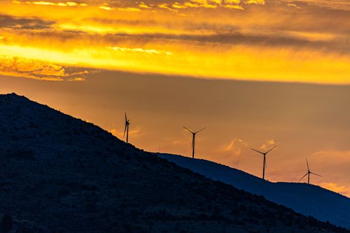 A scenic shot of a windmill farm up in the mountains with the evening golden sky illuminated