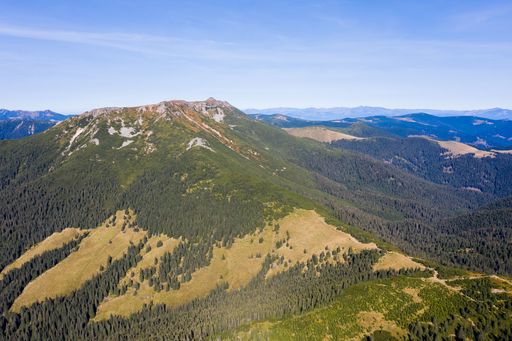 Stunning view of layered mountain ranges covered with dense pine forest and green valley under blue sky on sunny day