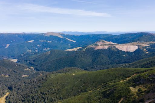 Stunning view of layered mountain ranges covered with dense pine forest and green valley under blue sky on sunny day