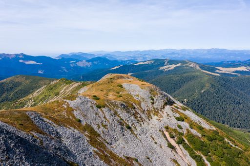 Stunning view of blue cloudy sky over layered mountain ranges and valley covered with vegetation on sunny day