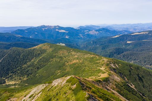Stunning view of blue cloudy sky over layered mountain ranges and valley covered with vegetation on sunny day