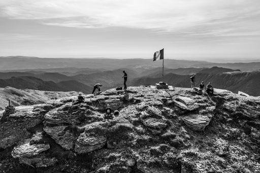 A black and white shot of group of hikers near the flag on the top of rocky mountain