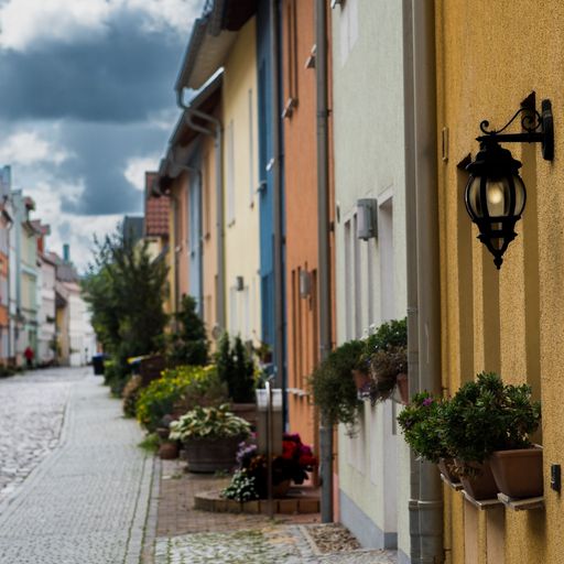 A street with a row of colorful houses decorated with flowerpots and a wall light in the foreground