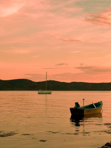 A vertical shot of boats in a sea during the sunset