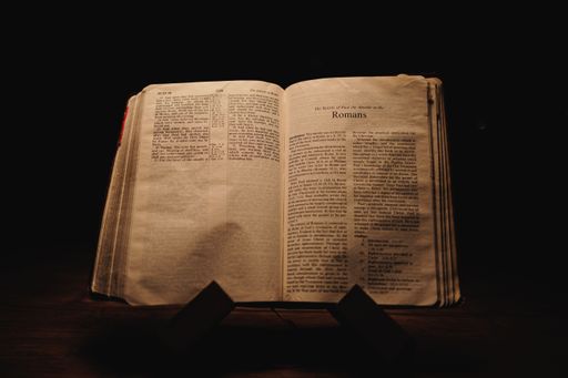 A closeup shot of a historic old Bible open on the Romans pages on display in a dark room