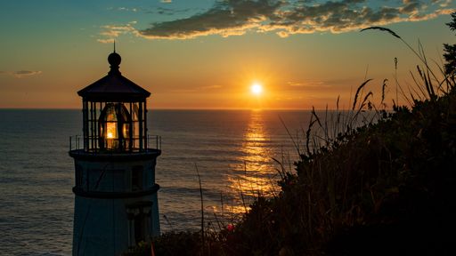 A silhouette of a lighthouse by a beach during the sunset