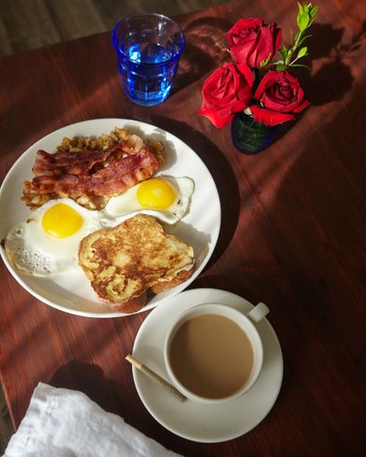 A vertical high angle shot of breakfast with eggs and bacon in a plate and a cup of coffee