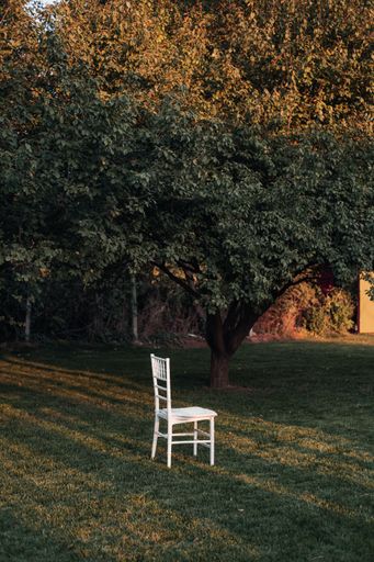 A vertical shot of a white empty chair on the green lawn.