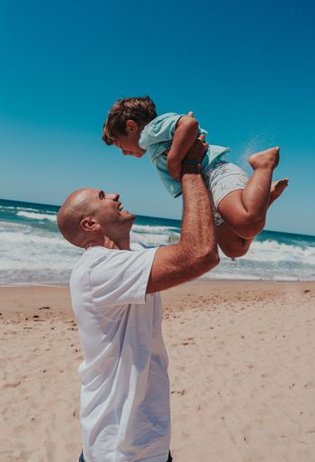 A vertical shot of a happy dad with his toddler son playing on a sandy ocean beach