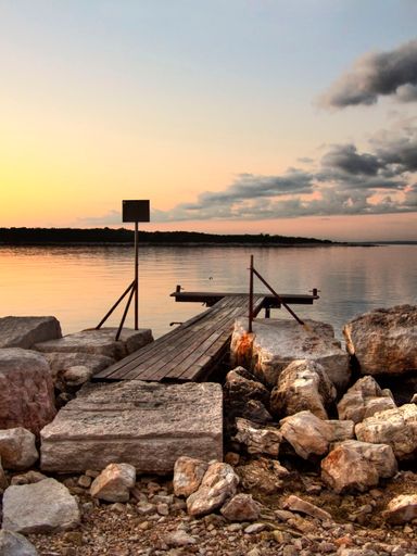 A vertical shot of a wooden pier on a rocky shore in the sunset