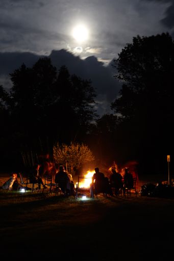 A vertical shot of a group of people sitting around a bonfire in the forest at night