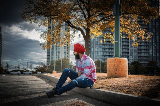 A South Asian male sitting on the edge of a road and looking away