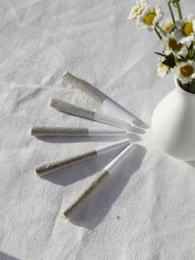 A vertical high angle shot of marijuana blunts and a vase of chamomiles on a white surface