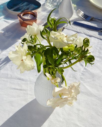 A vertical high angle shot of a vase with beautiful white flowers on a table with a white tablecloth