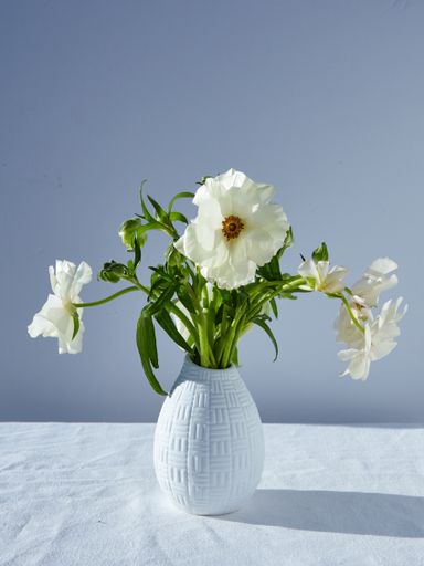 A vertical closeup shot of a vase with beautiful white flowers with a gray background