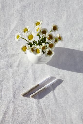 A vertical overhead shot of a vase of chamomiles on a table with a white tablecloth