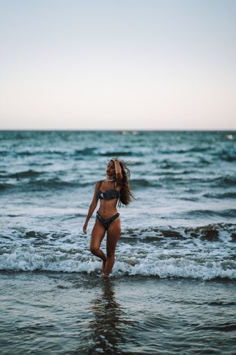 A sexy caucasian woman with a fit slim body wearing a bikini swimsuit and posing standing in a seawater