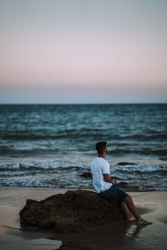 An amazing shot of a man sitting on a beach rock and enjoying a beautiful seascape view