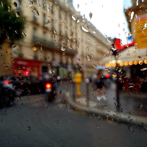 A vibrant street scene of Paris through the window with water droplets.