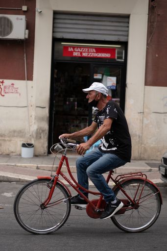 A vertical shot of an old man cycling a red bike in Bari, Italy