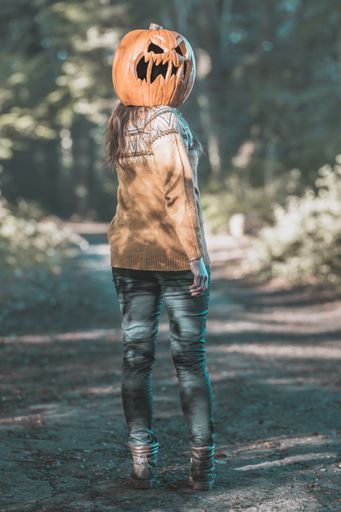 A vertical shot of a young woman wearing a pumpkin on her head in the forest