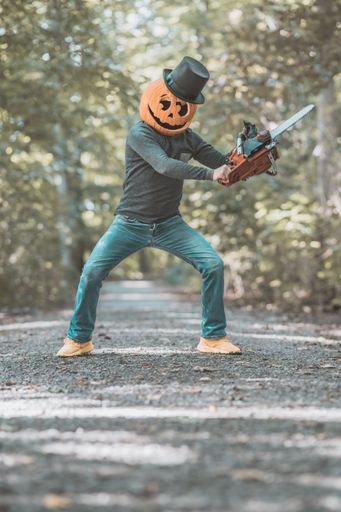 A vertical shot of a young boy wearing a pumpkin on his head in the forest