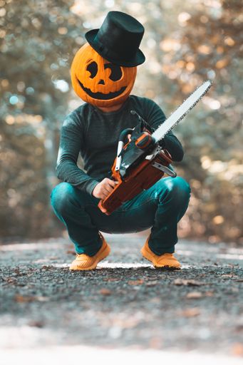 A vertical shot of a young boy wearing a pumpkin on his head in the forest