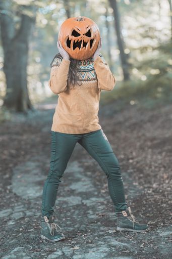 A vertical shot of a young woman wearing a pumpkin on her head in the forest