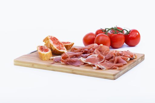 A closeup shot of delicious slices of typical Spanish ham next to some bread and tomatoes on a wooden cutting board