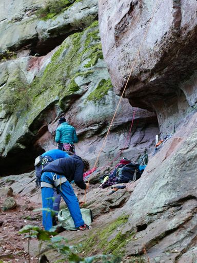 A vertical shot of people preparing their harnesses on the side of a rock mountain