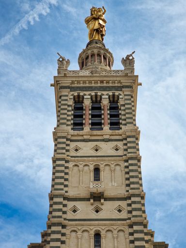 The low-angle view of Basilique Notre-Dame de la Garde tower against the cloudy blue sky