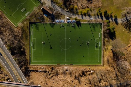 An aerial view of football fields surrounded by nature and next to a road