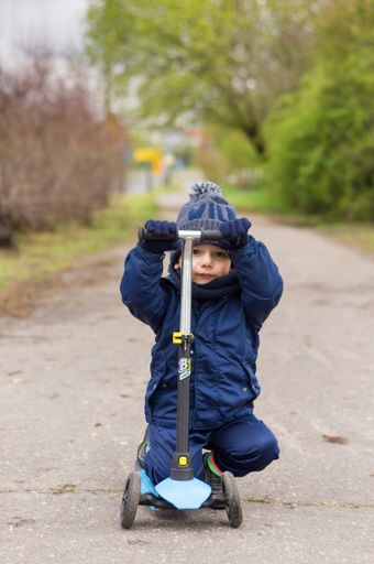 Little boy riding a scooter on a footpath on a cold day