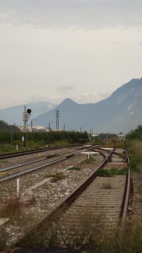 A vertical shot of railway tracks with mountains in the background under a cloudy sky