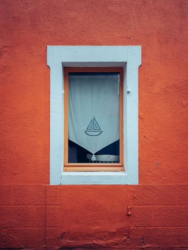 A vertical shot of a white window of an orange building with a boat on a curtain in Nantes, France