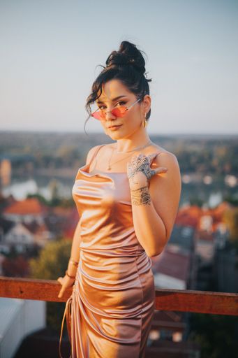 A vertical shot of a sexy Caucasian white woman in a silk dress and sunglasses on the balcony