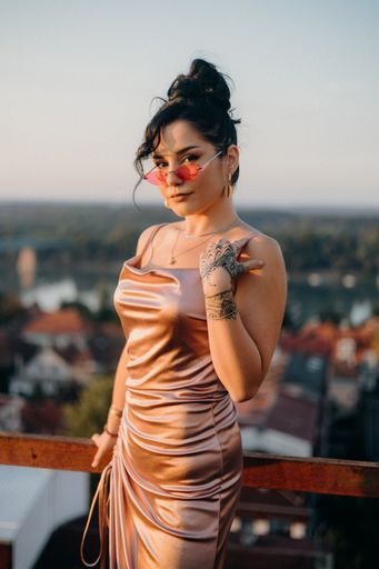 A vertical shot of a sexy Caucasian white woman in a silk dress and sunglasses on the balcony