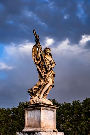 A vertical shot of a marble angel statue holding the cross on the St. Angelo Bridge under cloudy sky in Rome, Italy