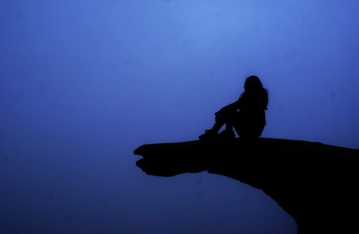 A beautiful shot of a silhouette of a female sitting on a rock with a blue background