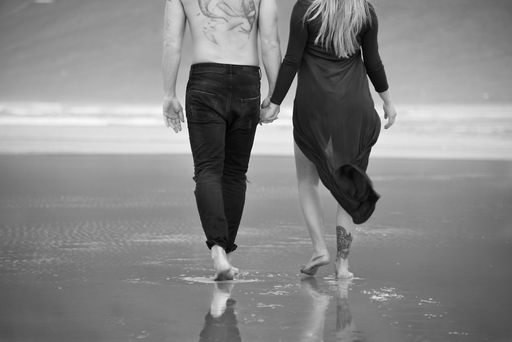 A romantic couple holding each other's hands and walking on the sandy beach towards the ocean waves