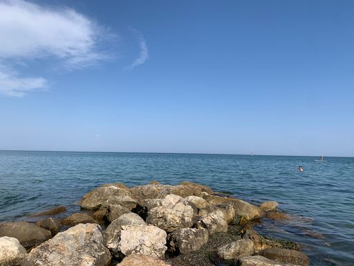 A scenic view of a blue ocean with big rocks on the beach in clear sky background in daylight