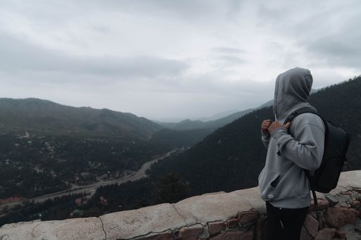 A male hiker on the top of pikes peak in Colorado looking to green mountains under gray foggy sky