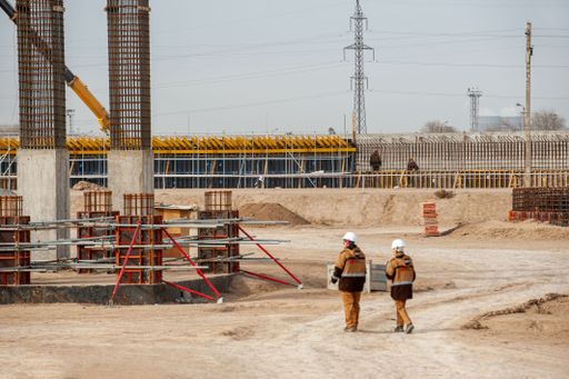 Two workers in special equipment and white helmets with a huge factory construction in the background