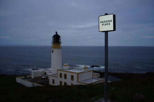 A Passing Place sign above the Neist Point lighthouse in Scotland with the sea in the background