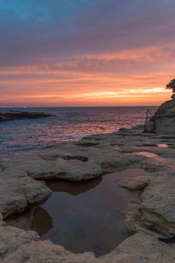 A vertical shot of a natural sea pool on the rocky beach under beautiful cloudy dusk sky