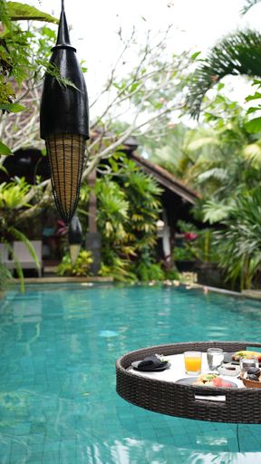 A vertical shot of a round tray with food and drinks in the pool floating on the water's surface.