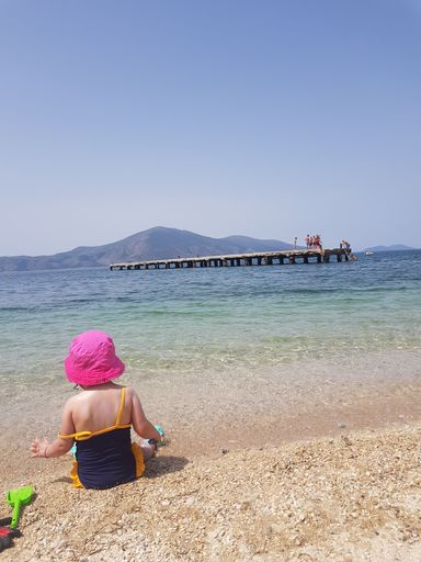 A vertical shot of a little girl sitting on the sand at the beach.