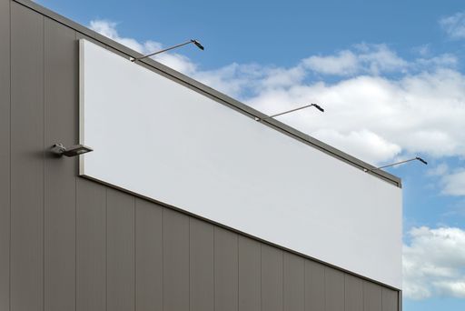 A big blank billboard on a gray building with the bright cloudy sky in the background