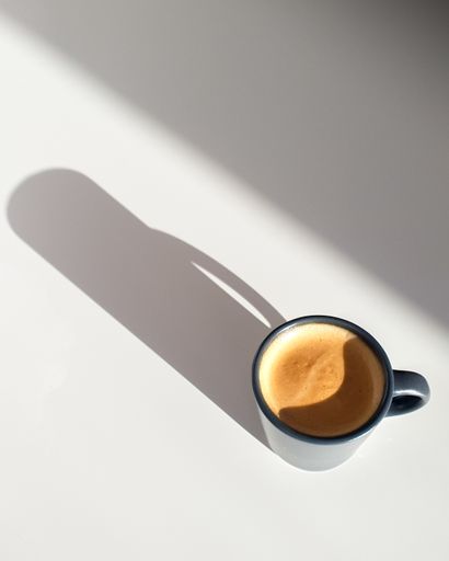 A high angle shot of a cup of coffee on a white surface under the lights